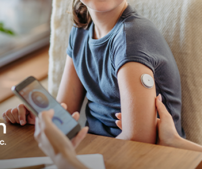 Mom holding daughter's arm that has a continuous glucose monitor on it and her phone with the tracking app in the other hand