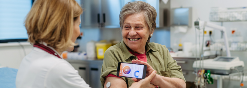 Senior woman smiling at doctor and showing her CGM app with CGM on her arm