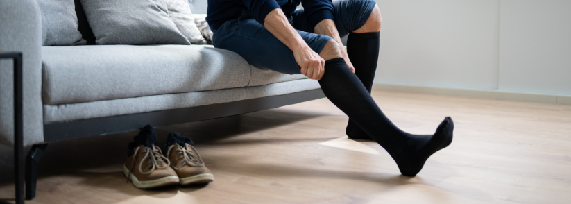 Man seated on the couch pulling on black compression stockings